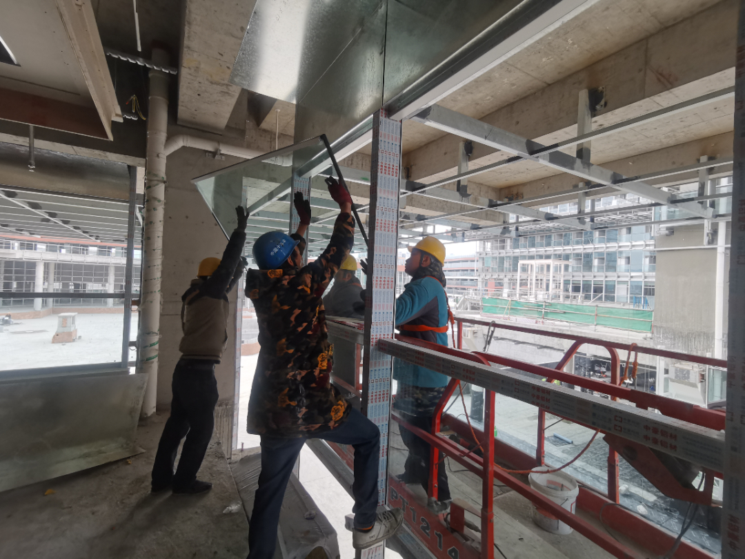  工人们正在进行幕墙玻璃安装。