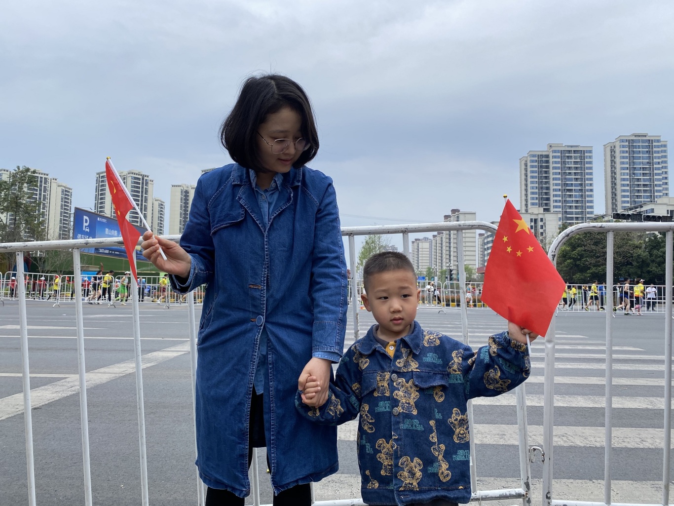 东坡大道与齐通路路口，一对母子挥舞五星红旗为参赛选手加油鼓劲。.jpg